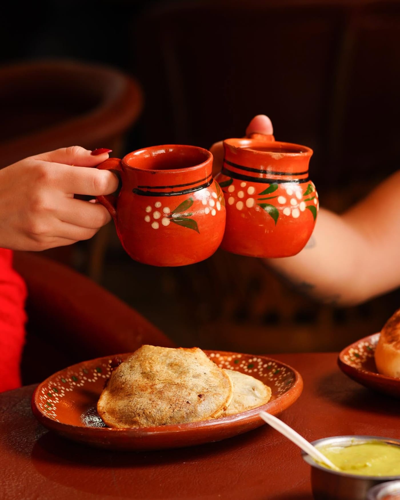 Dos jarros de café de olla brindando, con una gordita en la mesa